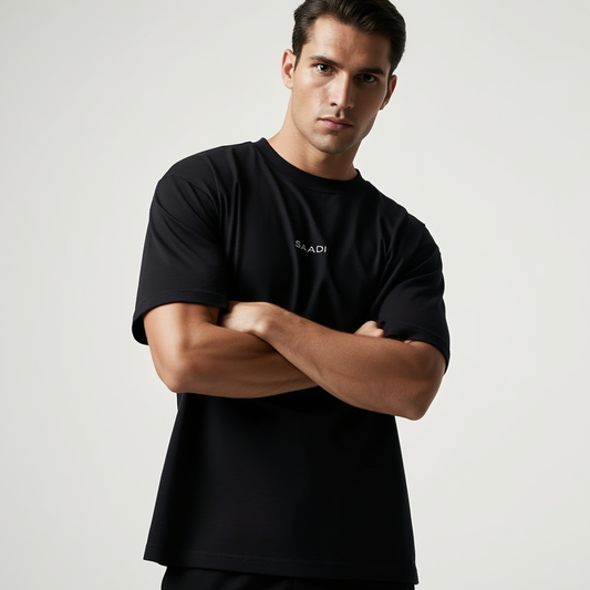 Man wearing a black t-shirt with a brand logo on a light gray background