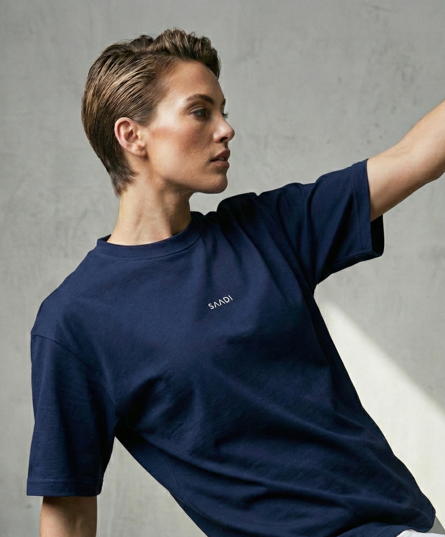 Person wearing a navy blue t-shirt with a brand logo, sitting against a neutral background